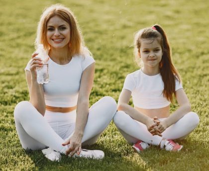 Smiling mother and daughter wearing matching outfits sitting on grass in a park.
