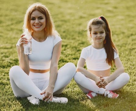 Smiling mother and daughter wearing matching outfits sitting on grass in a park.