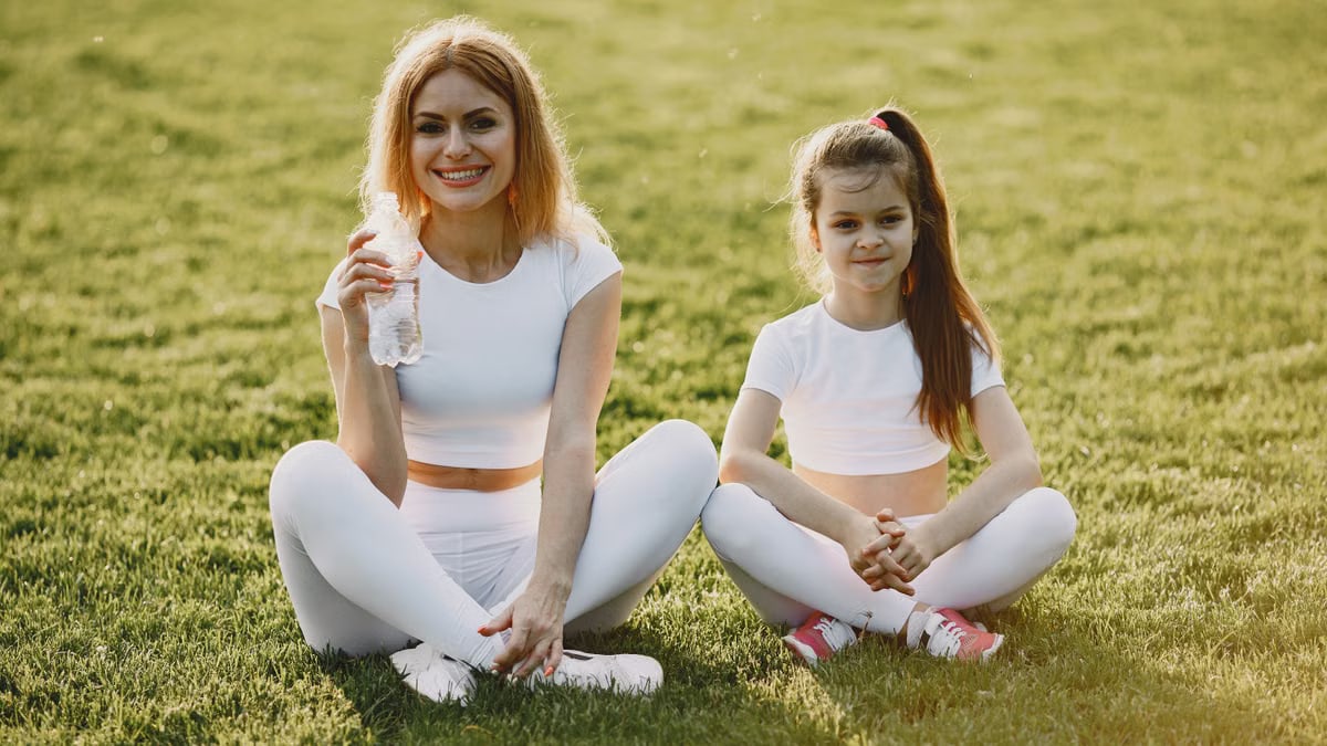 Smiling mother and daughter wearing matching outfits sitting on grass in a park.
