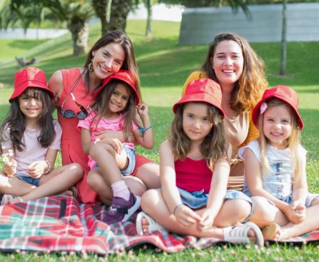 Friends enjoying a sunny day picnic on grass with bucket hats and smiles in a Portuguese park.