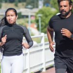 Active couple jogging outdoors on a sunny day, promoting fitness and healthy lifestyle.